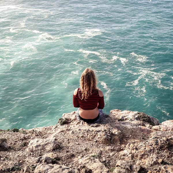Lisa Rossmann von hinten fotografiert, wie sie auf Felsen über dem türkisblauen Meer sitzt.
